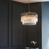 Endon Beaumont 5 light pendant in brass with tiered clear glass rods, hanging from a chain against a dark panelled wall in a living space.