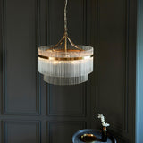 Endon Beaumont 5 Light Pendant in brass with tiered clear glass rods and chain suspension, hung against a dark panelled wall above a side table.