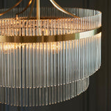 Close-up of the Endon Beaumont 5 Light Pendant in brass, showing tiered clear glass rods around a brushed brass band with lit E14 lamps inside.
