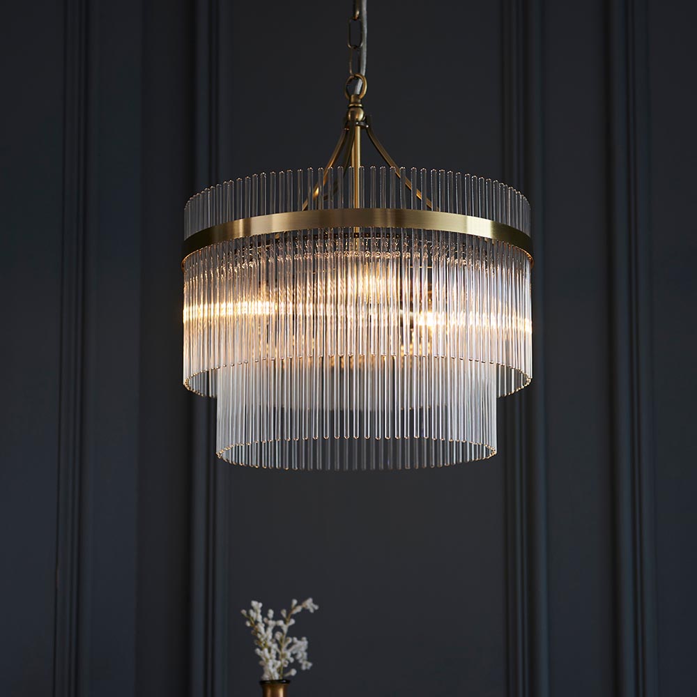 Endon Beaumont 3 Light Pendant in brass, a two-tier chandelier with clear glass rods and chain suspension, shown against a dark panelled wall.