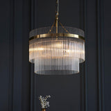 Endon Beaumont 3 Light Pendant in brass, a two-tier chandelier with clear glass rods and chain suspension, shown against a dark panelled wall.