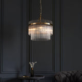 Endon Beaumont 3 Light Pendant in brass with two tiers of clear glass rods, illuminated above a small side table against a dark panelled wall.