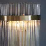 Beaumont Wall Light in brass, close-up of clear glass rods lit from within, with a brushed brass band and backplate against a grey background.