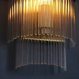 Beaumont Wall Light in brass, close-up of clear glass rods cascading from a brass backplate, glowing warmly against a dark background.