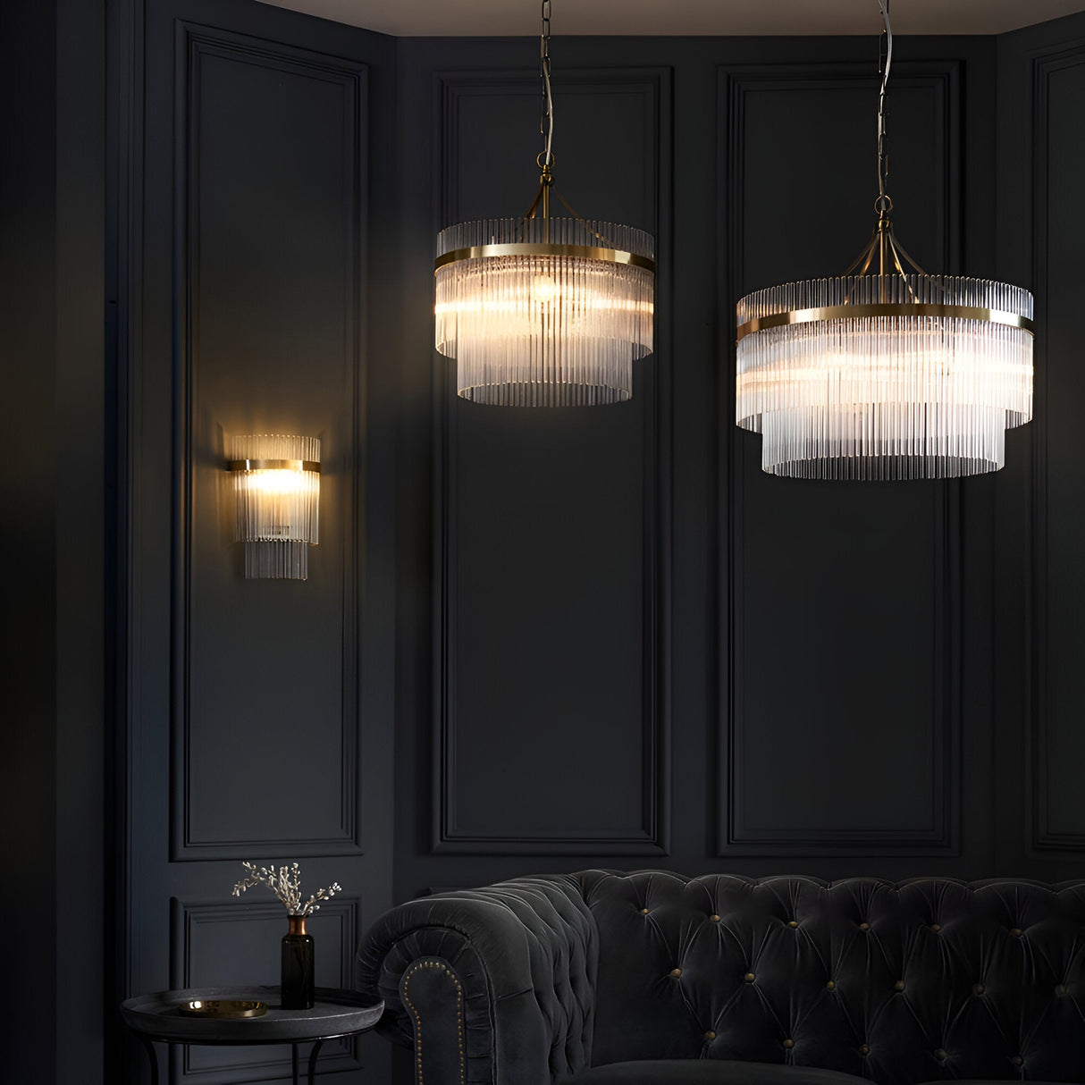 Beaumont Wall Light in brass with clear glass rods, illuminated on a dark panelled wall beside matching pendant lights in a living room setting.