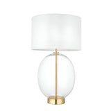 Brockmere Table Lamp with oversized oval clear glass base, satin brass stem and base plate, and white fabric drum shade on a plain white background.