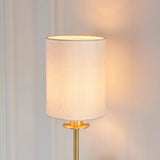 Endon Cliffhurst wall light with a slim satin brass upright and vintage white cylinder shade, illuminated against a pale panelled wall.
