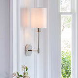 Endon Cliffhurst wall light with a slim polished nickel arm and vintage white cylinder shade, mounted on a panelled wall beside a bright window.