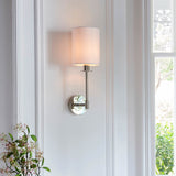Endon Cliffhurst wall light in polished nickel with a slim upright, round backplate and vintage white cylinder shade, mounted on a white panelled wall.
