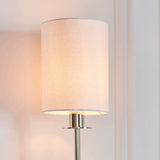 Endon Cliffhurst wall light illuminated on a panelled wall, featuring a slim polished nickel upright and a vintage white cylinder fabric shade.