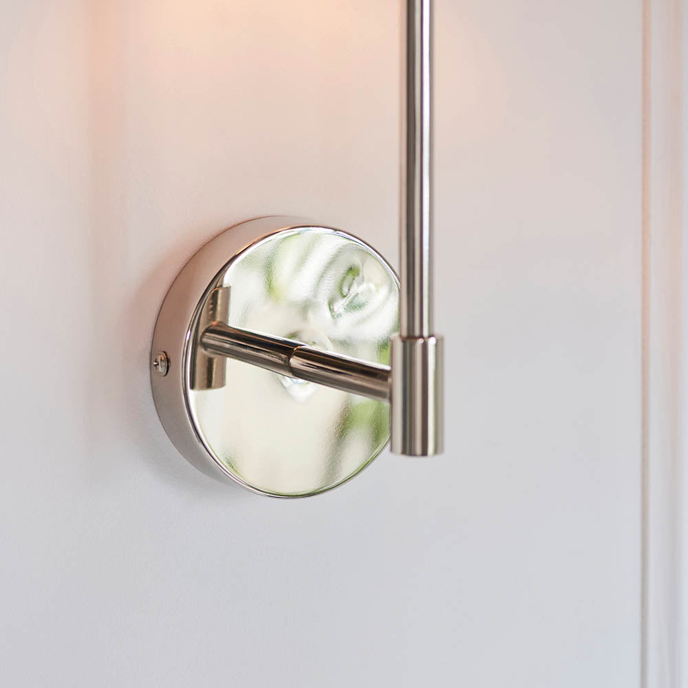 Close-up of the Endon Cliffhurst wall light in polished nickel, showing the round wall plate, slim upright and cylindrical fitting against a white wall.
