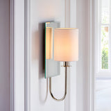 Endon Carlhurst wall light with bevelled mirrored backplate, polished nickel curved arm and vintage white fabric cylinder shade, mounted between windows.