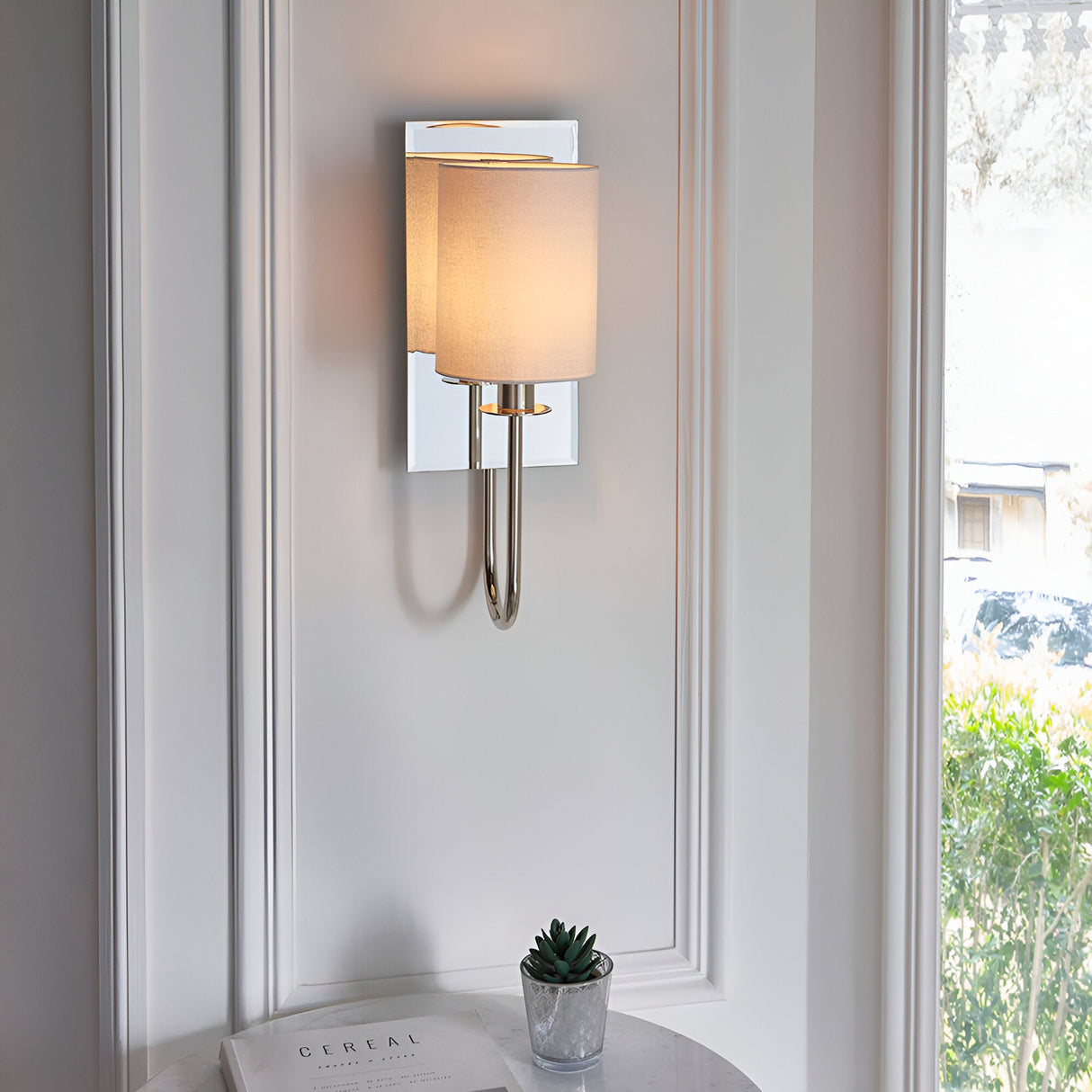 Endon Carlhurst wall light with bevelled mirrored back plate, polished nickel arm and vintage white fabric cylinder shade, mounted beside a window.