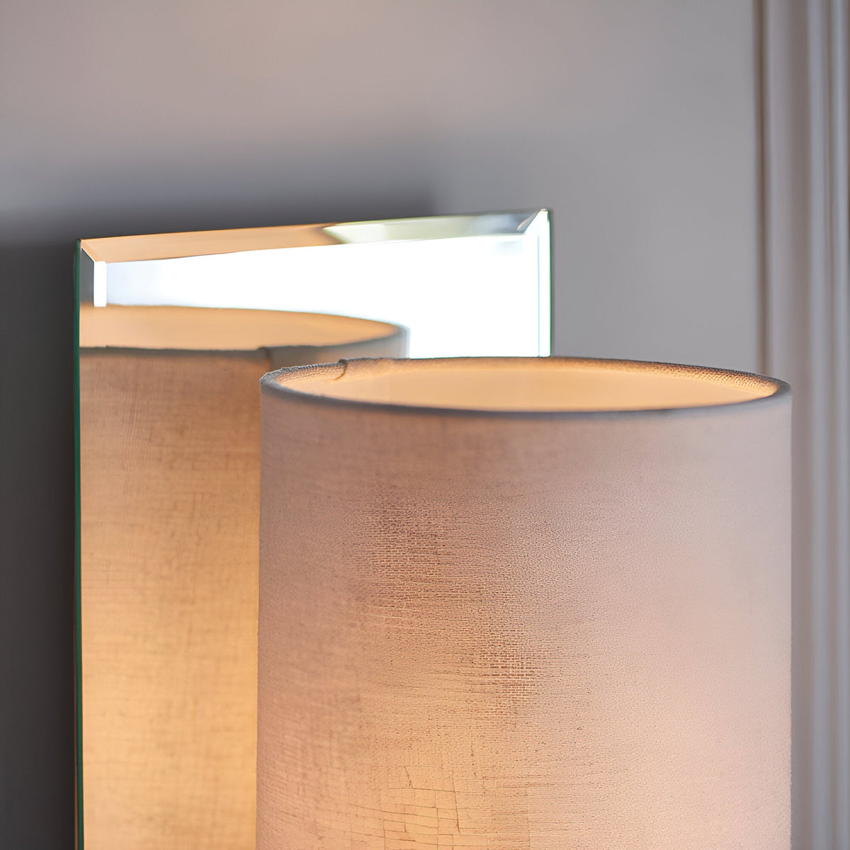 Endon Carlhurst wall light with bevelled mirrored back plate, polished nickel arm and vintage white fabric cylinder shade, shown illuminated.