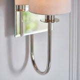 Close-up of Endon Carlhurst wall light showing polished nickel curved arm, bevelled mirrored back plate and vintage white fabric cylinder shade.