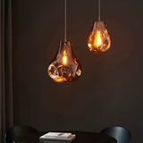 Two Brackwell copper glass pendant lights with organic molten shapes and chrome fittings, hanging above a black dining table.