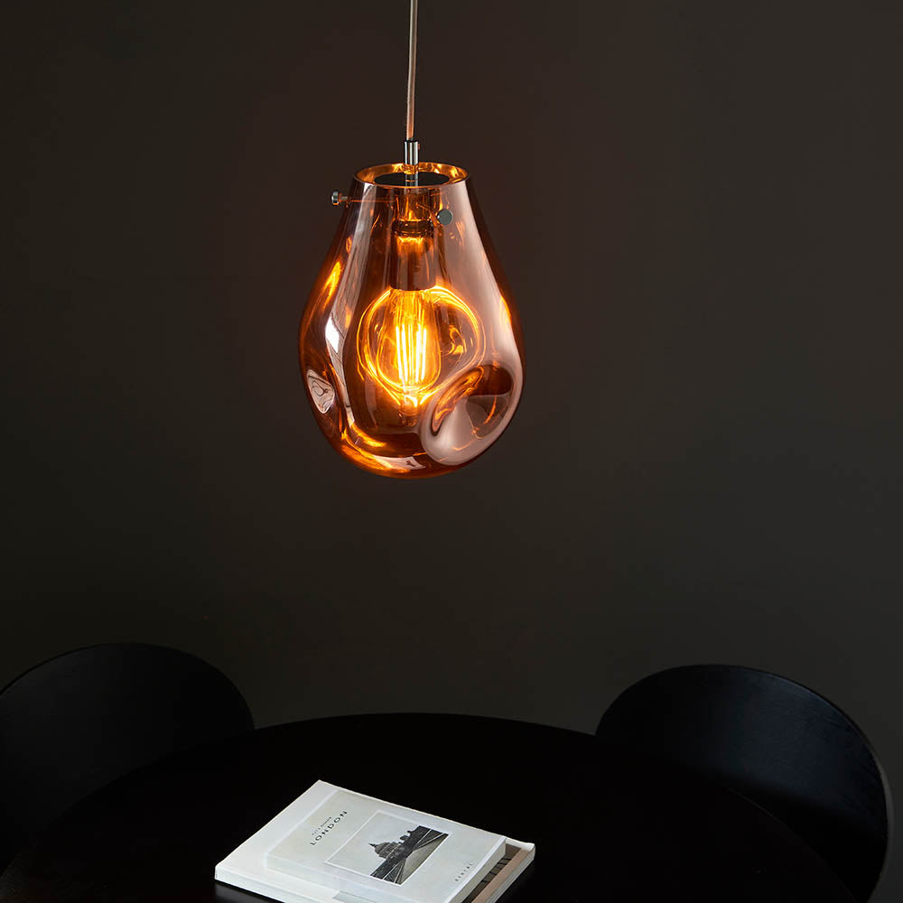 Brackwell Glass Pendant in Copper, a single-light fixture with an organic molten glass shade and chrome fittings, shown lit above a dark dining table setting.