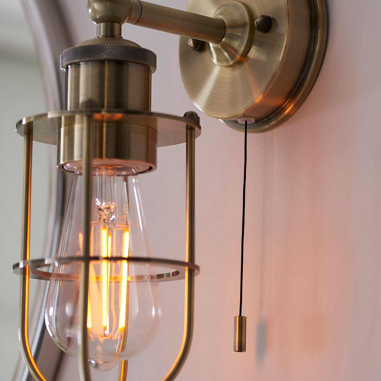 Bevwood industrial-style bathroom wall light in brass, with cage shade, knurled detailing, wall mount, and pull cord switch, IP44 rated.