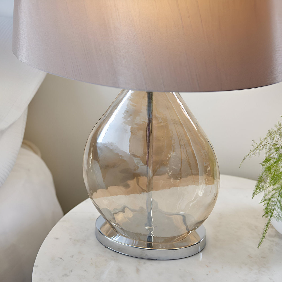 Brockstead Table Lamp with gold-tinted dimpled glass base, chrome metalwork, and mink oval shade, shown lit on a bedside table.