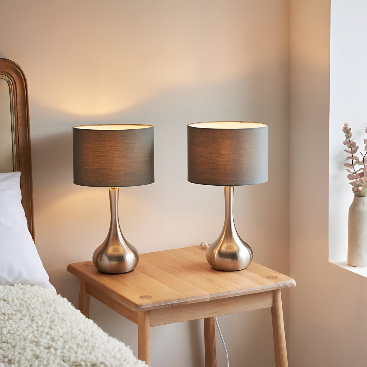 Endon Chartbury LED table lamps in a twin pack, with satin nickel teardrop bases and grey drum shades, lit on a wooden bedside table.