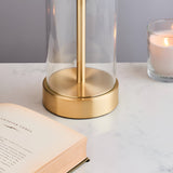 Close-up of Endon Caldley table lamp brass base with clear cylindrical glass, on a marble surface beside an open book and lit candle.