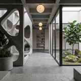 A modern, minimalist interior with concrete walls, geometric partitions, potted plants, and large glass windows overlooking a Zen garden. Lunar Flush Ceiling Light - White fixtures provide ambient lighting along the hallway.