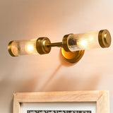 Akurdi 2 Light Bathroom Wall Light in Clear, showing two ribbed glass cylinders with brass caps mounted horizontally on a brass wall plate above a framed picture.
