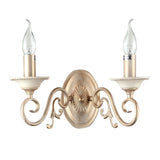 The Perla 2 Light Classic Wall Light features a vintage-inspired design with two candle-shaped bulbs on gracefully curved arms and a decorative backplate, all in a soft gold finish.