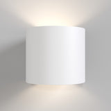 The Rond Up & Down Wall Light - White features a sleek, cylindrical design mounted on a light wall. Its minimalist style emits soft light from both ends, creating an ambient glow. The matte white finish lends elegance to any space.