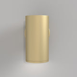 The FOCUS S Down Wall Light, in matte gold, mounted on a light gray wall, emits a subtle glow above and below. Its sleek and minimalist design with clean lines and a smooth surface brings an industrial-inspired touch to customizable lighting solutions.