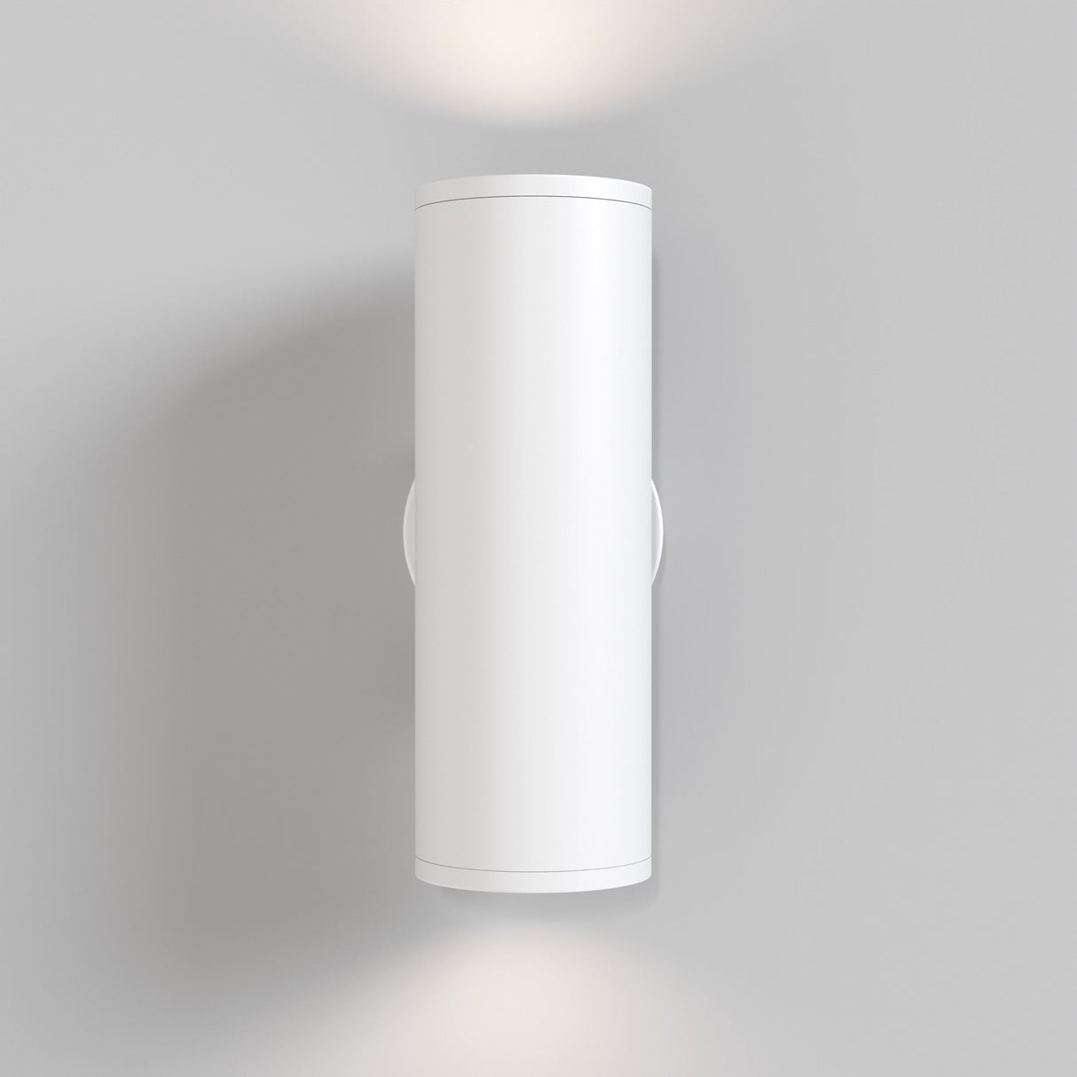 The FOCUS S Up & Down Wall Light in white, with a modern cylindrical design, elegantly mounts on a light gray wall. Its GU10 bulbs softly illuminate the space above and below, creating a refined ambiance.