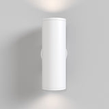 The FOCUS S Up & Down Wall Light in white, with a modern cylindrical design, elegantly mounts on a light gray wall. Its GU10 bulbs softly illuminate the space above and below, creating a refined ambiance.