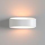 The Trame LED Wall Light 6W 3000K, in white, emits a soft, warm glow against a light gray wall. Its minimalist, modern design diffuses energy-efficient light both upwards and downwards, creating an elegant ambiance that embodies contemporary aesthetics.