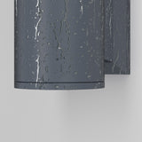 The Bowery Outdoor 1 Light Wall Light - Grey (O574WL-01GR) is a dark gray cylindrical fixture with a raindrop-textured surface, offering durability and elegance when mounted on a light gray wall.