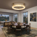 A modern dining room with a round wooden table for five and wooden chairs is illuminated by the Orbis Medium LED Alabaster Semi-Flush Ceiling Light – Soft White. Large windows, abstract art, and a view into the living area complete the space.