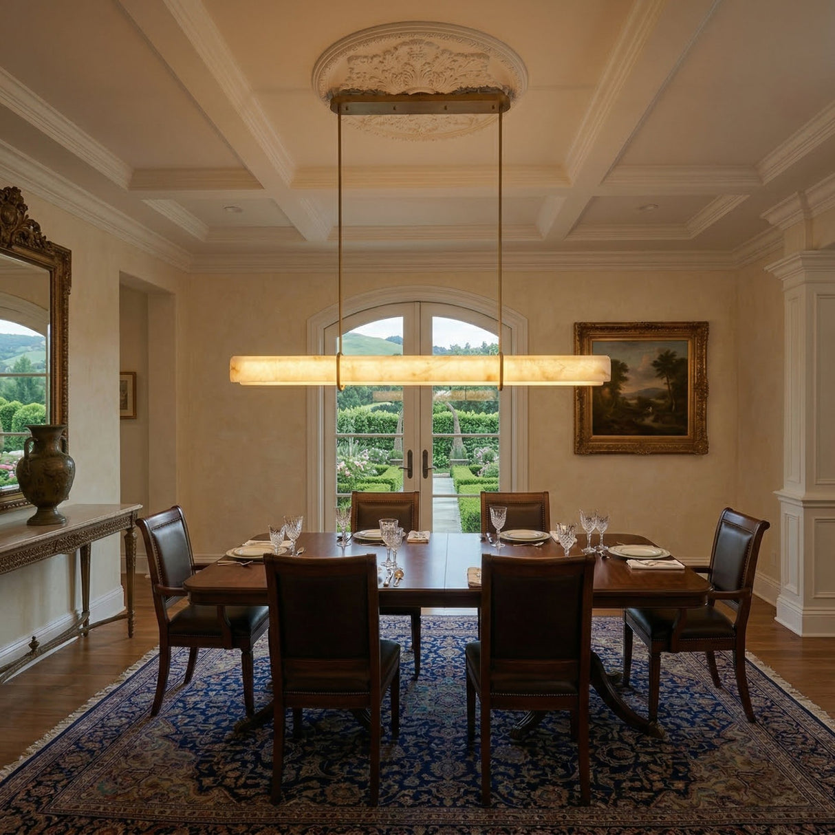 Niori Zarune linear alabaster chandelier in brushed brass hangs above a wooden dining table with leather chairs in a coffered-ceiling room.