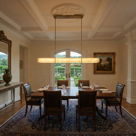 Elegant dining room with a wooden table for six, classic chairs, an ornate mirror, framed art, and French doors to the garden—illuminated by the Zarune LED Linear Drop Alabaster Suspension Light in brushed brass and soft white.
