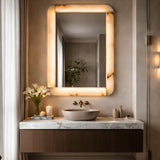 Niori Solviera LED alabaster rectangular wall mirror with brushed brass inlay and warm halo glow, mounted above a marble vanity with stone vessel sink.