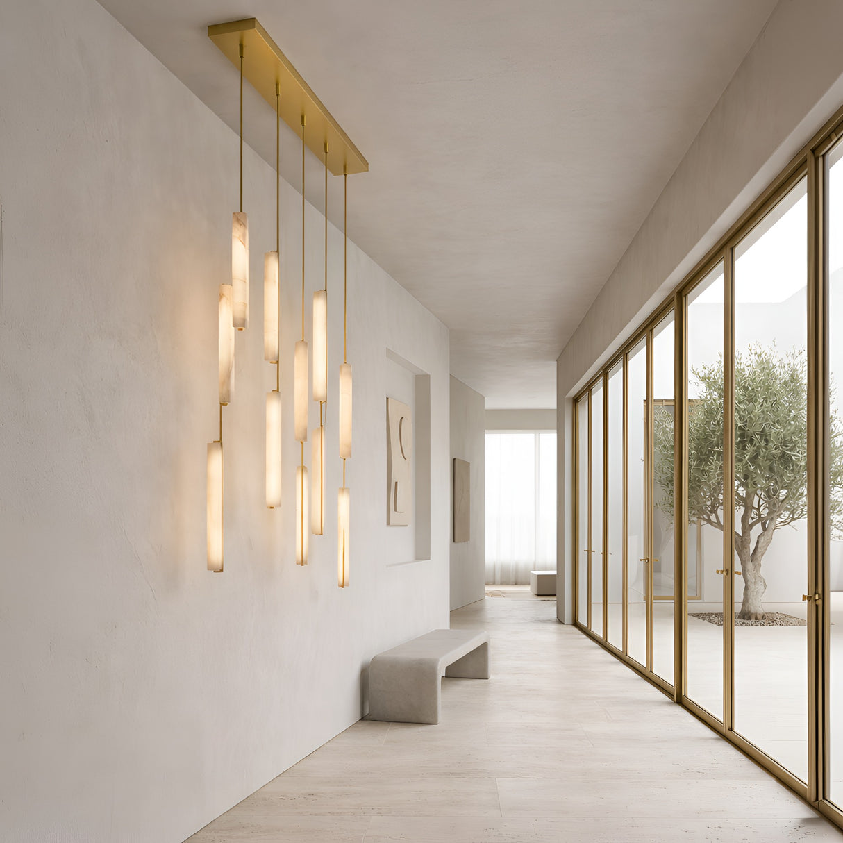 Niori Selvara 10 Light Vertical Alabaster Linear Chandelier with brushed brass canopy and staggered lit batons above a bench in a minimalist hallway.