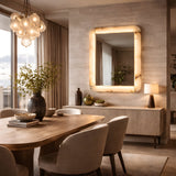 Niori Solviera LED alabaster rectangular wall mirror with soft white glow, mounted above a sideboard in a warm dining room with wooden table and beige chairs.