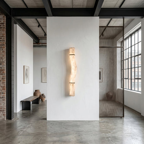 A modern, minimalist room with concrete floors, white walls, and large windows features the Zarune LED Sculpted Curve Alabaster Wall Light in Matte Black & Soft White as a centerpiece; pottery, a bench, and framed art complete the airy space.