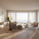 A bright, modern living room with a cozy sofa, unique wicker chairs, and a round coffee table. The Varelle Stacked Alabaster Floor Lamp in Soft White & Matte Black adds sculptural lighting near large glass doors overlooking the ocean.