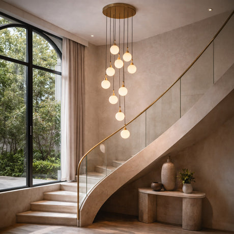 Niori Lorixa 9-light cascading chandelier with brushed bronze canopy and white alabaster globes, hung above a curved staircase beside an arched window.
