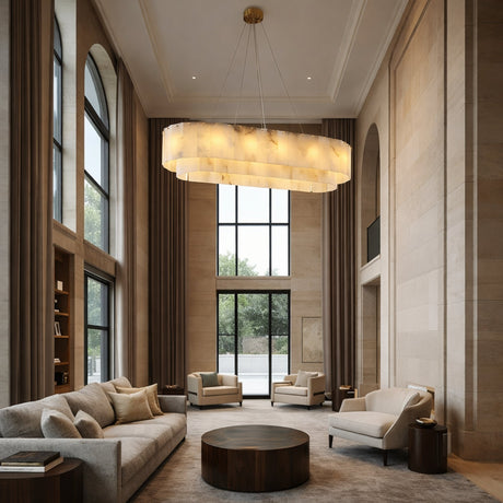 A spacious modern living room with tall windows, beige walls, and neutral furniture centers on the Arvello 12 Light Layered Panel Alabaster Linear Chandelier in Soft White & Brass. Two sofas and armchairs encircle a round coffee table on a gray rug.