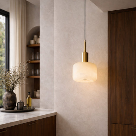 A modern kitchen with wooden cabinets, a marble countertop, a decorative vase with dried branches, and the Nerix 1 Light Large Drum Alabaster Single Pendant Light in Soft White & Brushed Brass softly illuminating the space.