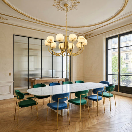 Elegant dining room with a long oval marble table, green and blue velvet chairs with gold frames, herringbone wood floor, ornate ceiling, tall windows and the Aurelio 10 Light Large Globe Alabaster Chandelier in Soft White & Brushed Brass.
