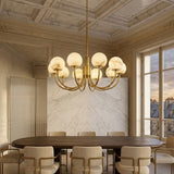 Elegant dining room with a dark oval table, cream upholstered chairs, the Aurelio 10 Light Globe Alabaster Chandelier in soft white & brushed brass, marble wall, coffered ceiling, and large windows framing a sunset cityscape.
