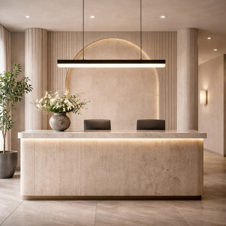 A modern, elegant reception desk with a marble-like finish, illuminated by the Linea LED Small Alabaster Linear Suspension Light in Soft White & Black. Features a vase of white flowers, two black chairs, neutral décor, and a potted plant on the left.