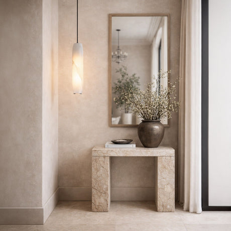 A minimalist entryway featuring a marble console, a ceramic vase with branches, a bowl, a book, a large wall mirror, the Vireth 1 Light Small Cylinder Alabaster Single Pendant Light in Soft White, soft beige walls, and sheer curtains by the window.