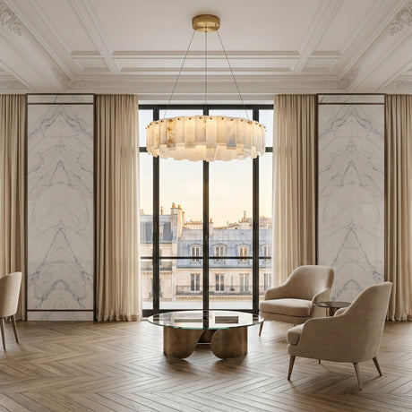 Elegant living room with large windows, beige armchairs, a round glass coffee table, cream curtains, chevron wood floor, and the Valeris 18 Light Layard Panel Alabaster Chandelier in Soft White & Brass; Parisian rooftops visible outside.